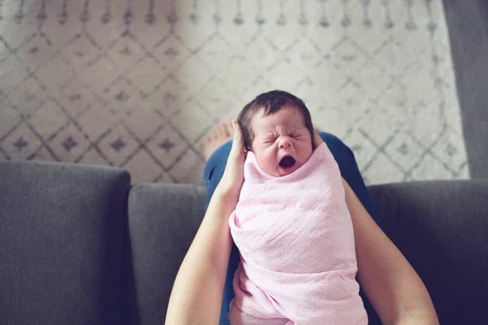 A person holding a crying newborn baby swaddled in a pink blanket.