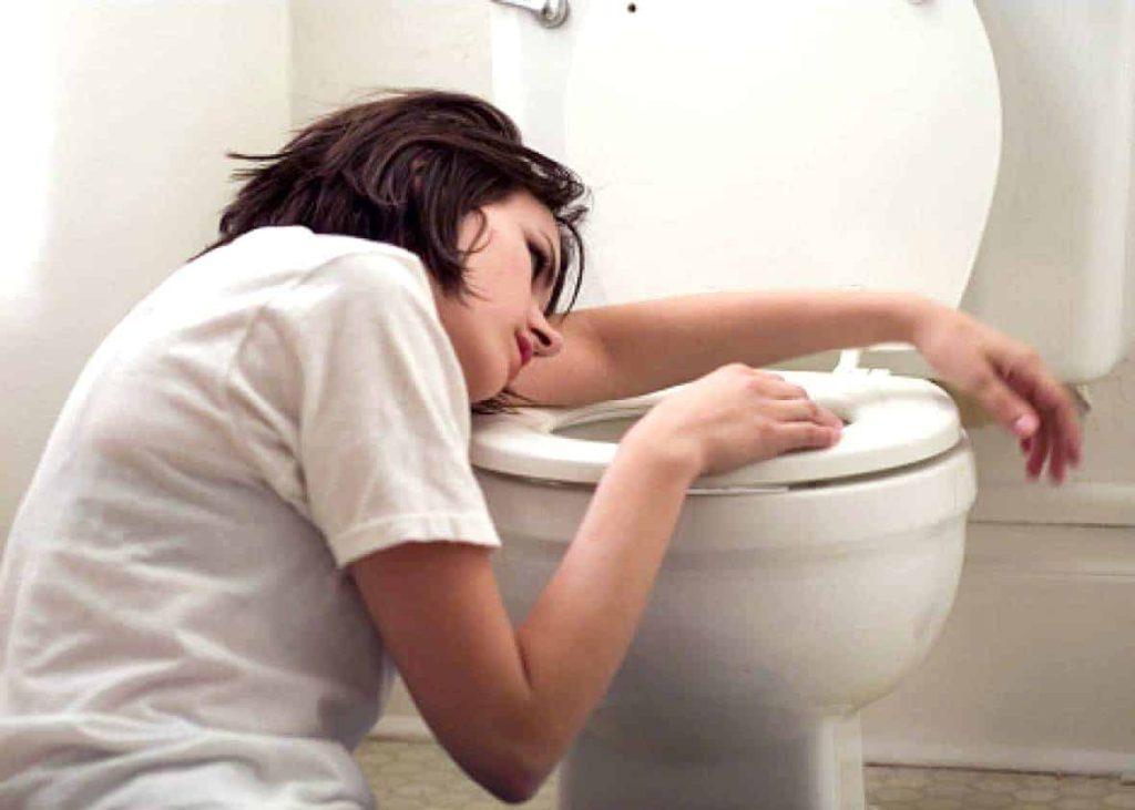 A woman with morning sickness leans over an open toilet in a bathroom.