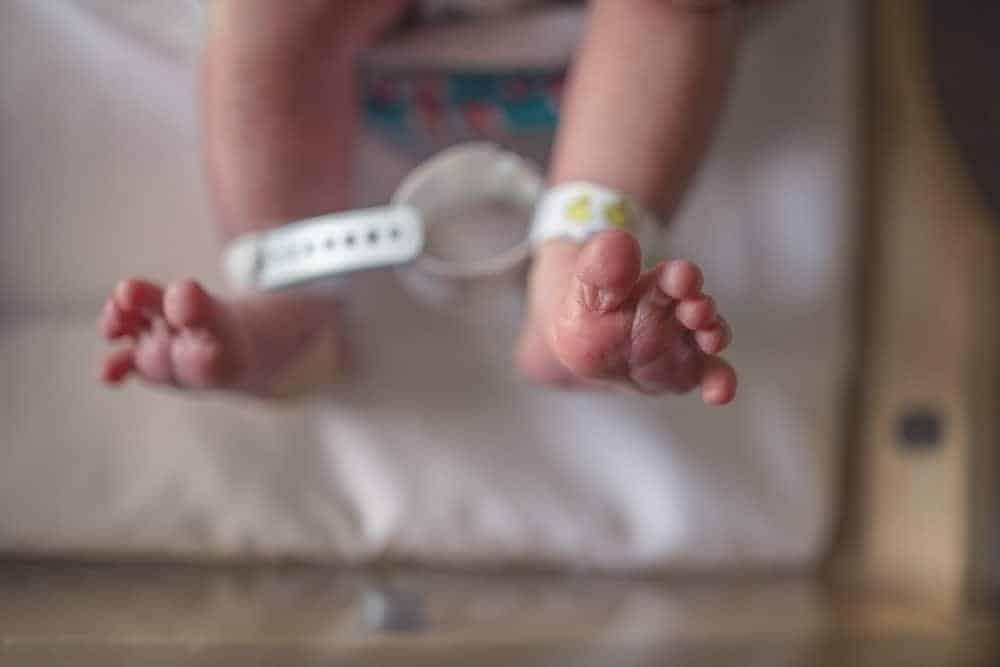 A newborn baby's feet with a white hospital identification band around one ankle.