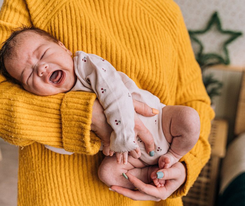 A person in a yellow sweater holding a crying newborn baby in their arms.