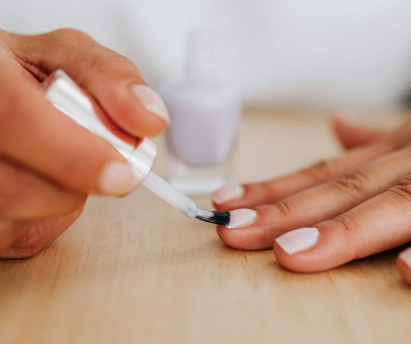 A hand brushes white nail polish onto a fingernail, reflecting the question of whether nail polish is safe during pregnancy and low-risk use.