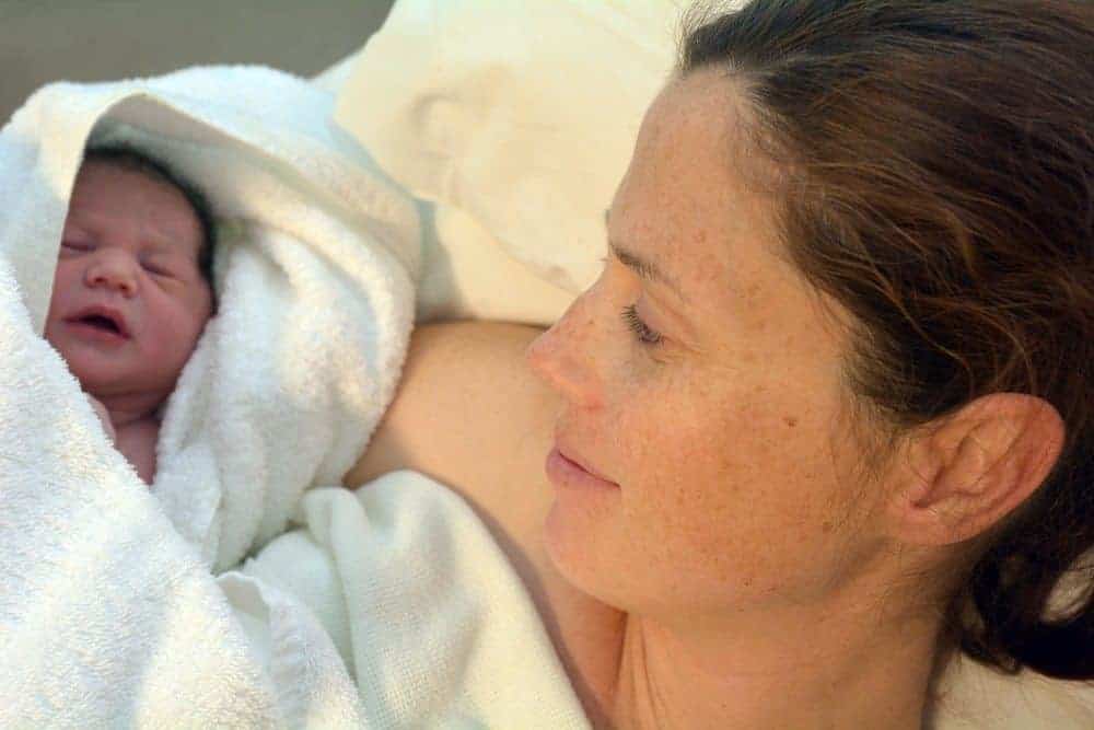A woman looking down at a newborn baby wrapped in a white towel.