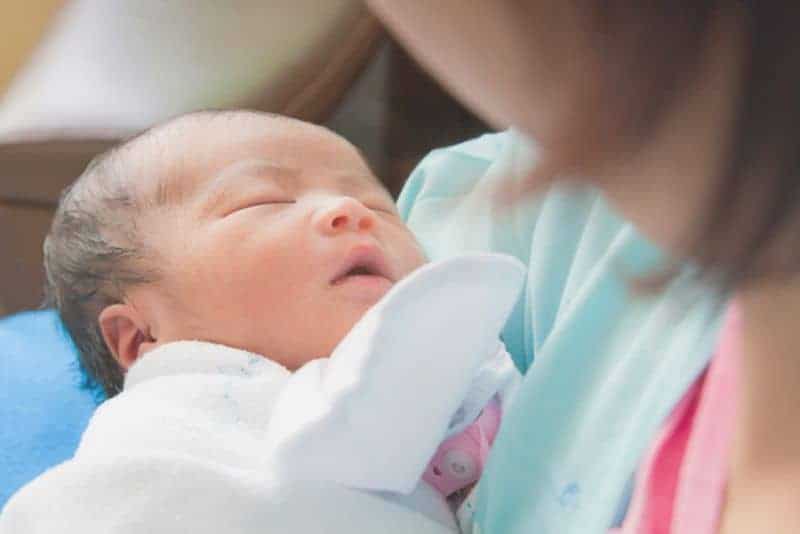 Close-up of a sleeping newborn baby held in the arms of their mother.