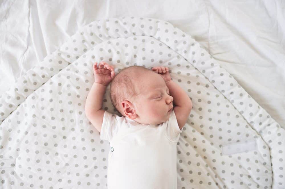 A sleeping newborn baby lies with arms raised on a white dotted blanket in a soft nursery-style setting, echoing the story of a one-off baby.