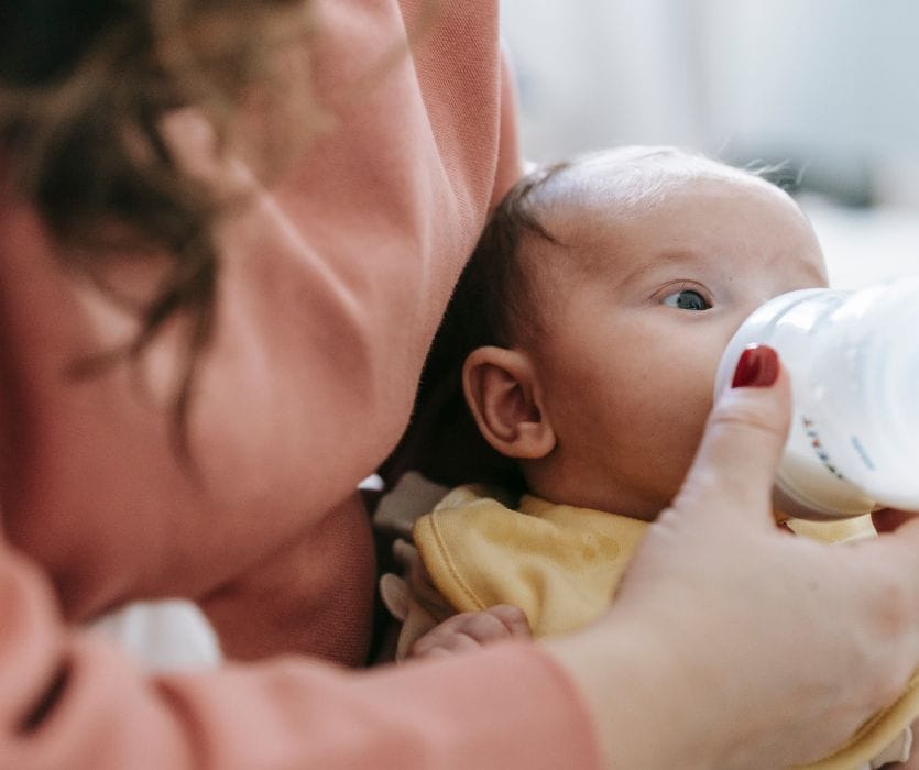Close-up of a baby being bottle-fed by an adult.