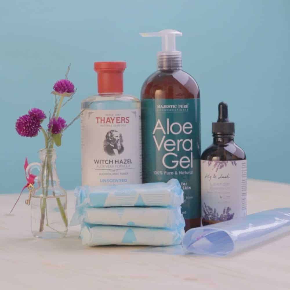 Thayers witch hazel, aloe vera gel, lavender essential oil, and a stack of sanitary pads on a wooden surface.