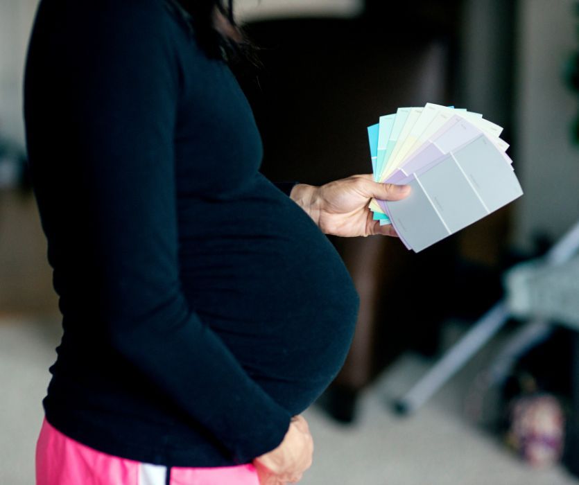 Side view of a pregnant person in a black long-sleeve shirt holding a fan of paint color swatches.