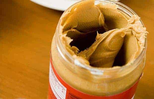 An open jar of creamy peanut butter with several large scoops missing.