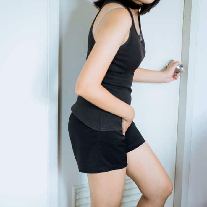 A person wearing black clothes holding their groin and reaching for a door knob.