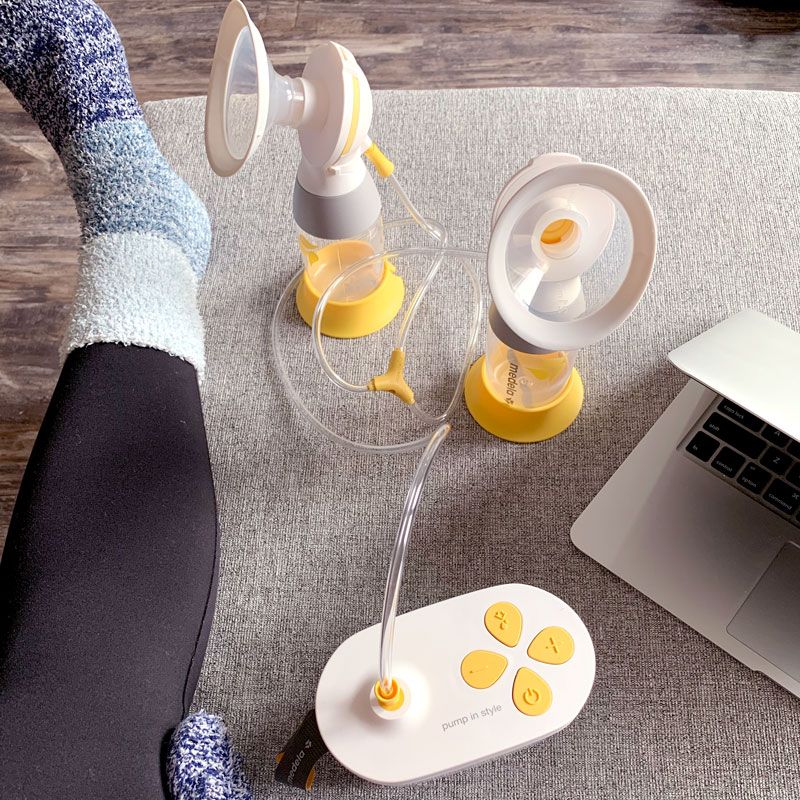 A Medela Pump In Style double electric breast pump with tubing and flanges on a gray surface next to a laptop.
