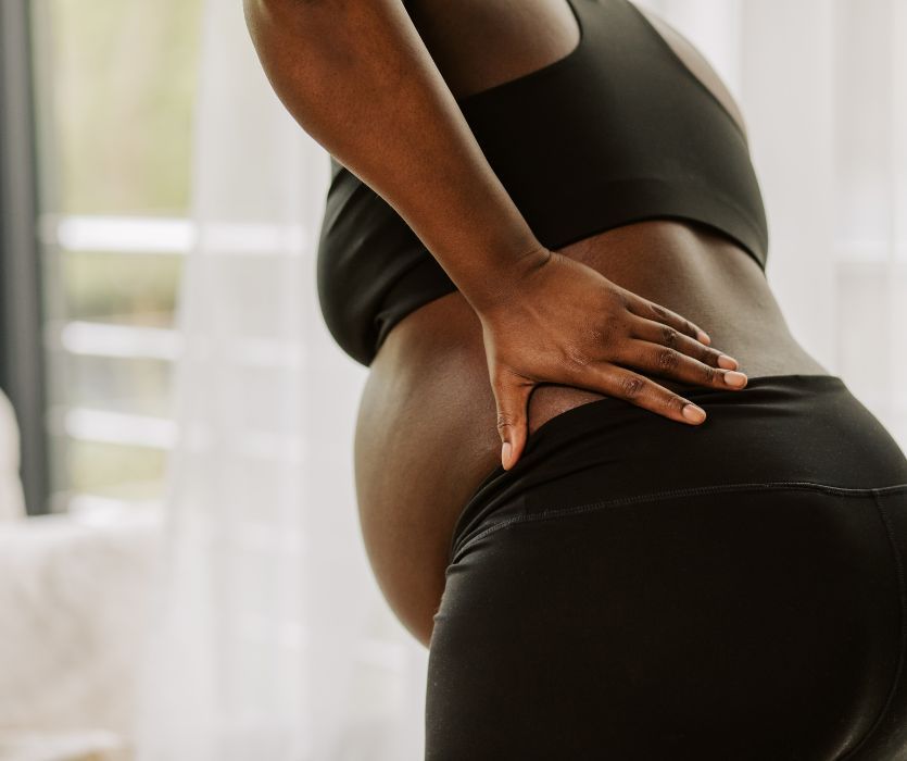 Side view of a pregnant person holding their lower back in discomfort.