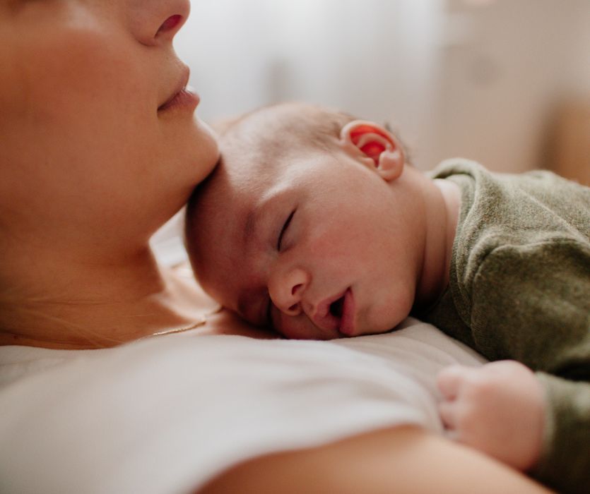 A close-up of a sleeping newborn baby resting their head on a woman's chest.