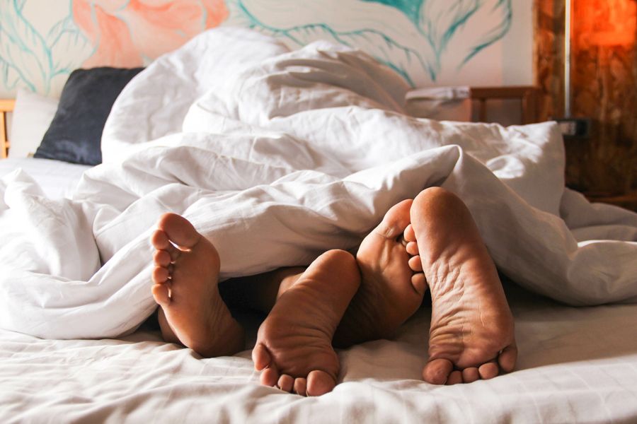 Two pairs of feet poking out from under a white duvet on a bed.