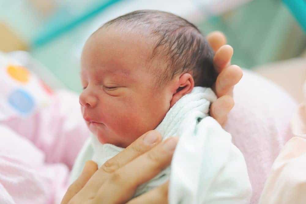 Close-up of a sleeping newborn baby swaddled in a white blanket and being cradled in a person's hands.