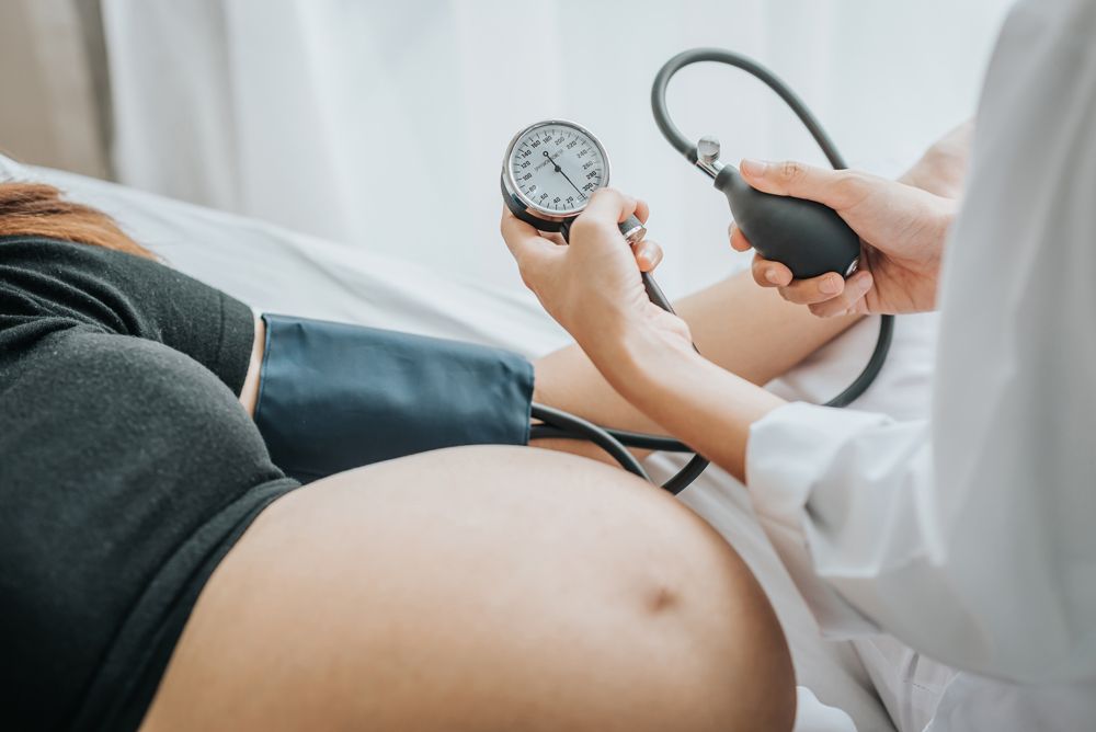 A doctor uses a manual sphygmomanometer to check the blood pressure of a reclining pregnant person.