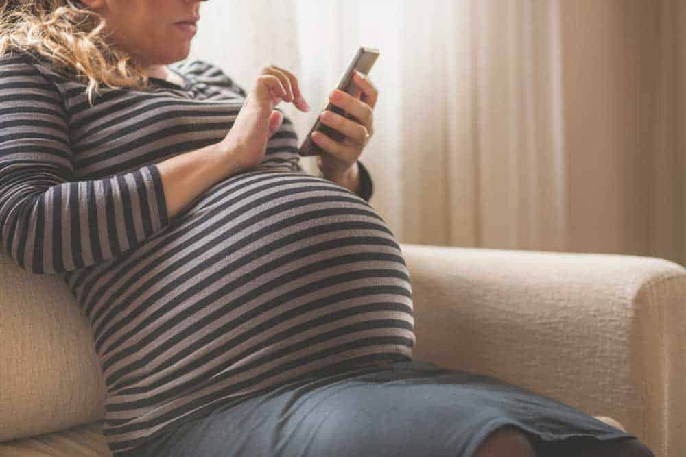 Pregnant woman in a striped shirt sitting on a sofa while using a smartphone.