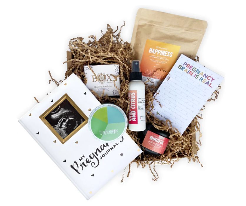 Pregnancy gift box with a journal, ultrasound photo frame, citrus spray, towelettes, and a notepad on shredded paper.