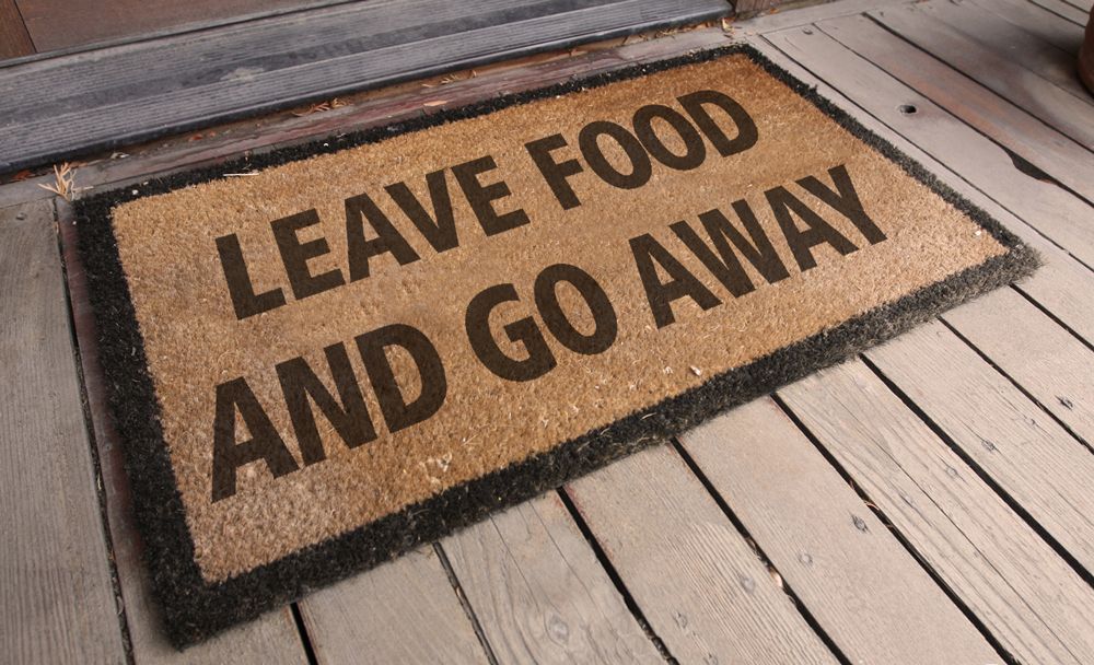 A brown coir doormat on a wooden porch with black text reading: Leave food and go away.
