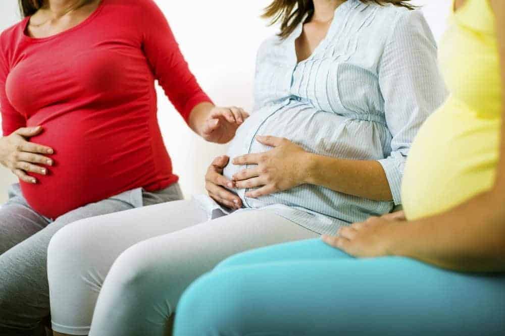 Three pregnant women sitting and holding their baby bumps.
