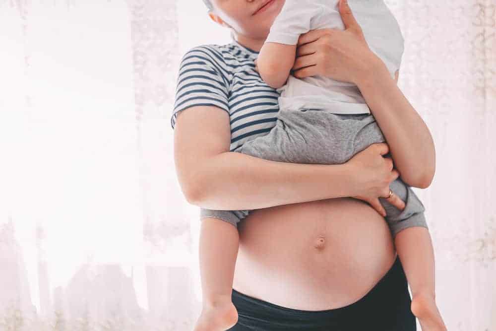 Pregnant woman holding her toddler son above her exposed belly.