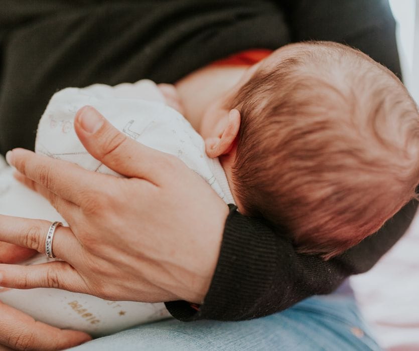 Close-up of a mother’s hand cradling a newborn baby’s head while breastfeeding.