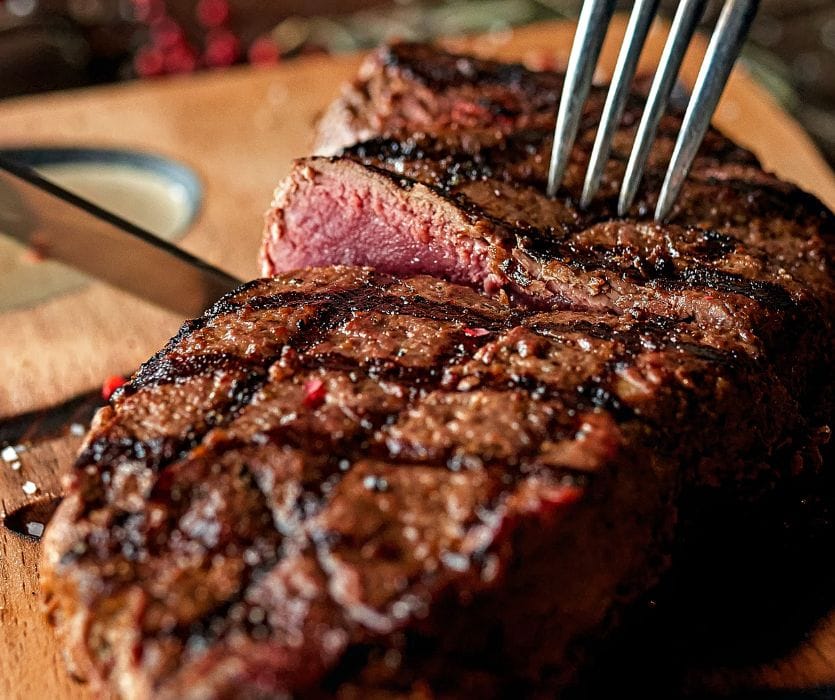 A grilled steak with a warm pink center and charred crust is cut open with a fork, reflecting guidance on medium-rare steak during pregnancy safety.