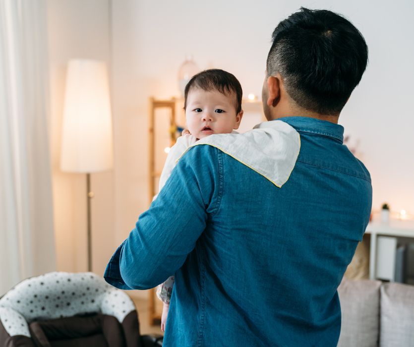 A man holding a baby over his shoulder with a burp cloth to manage infant reflux.