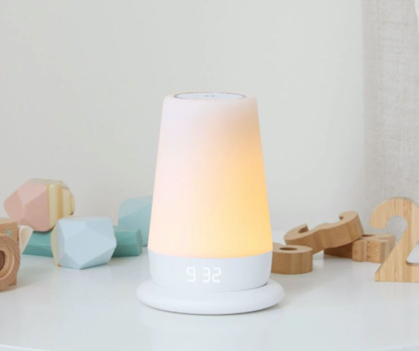 A tapered Hatch white noise machine and nightlight glowing warm orange, surrounded by pastel blocks and wooden numbers.