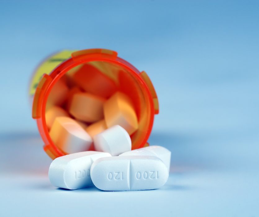 White oblong pills spilling out of an orange prescription bottle against a blue background.
