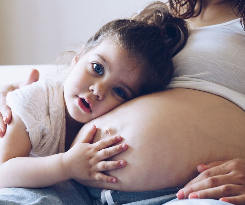 Young girl resting her head and hands on a woman's pregnant belly.