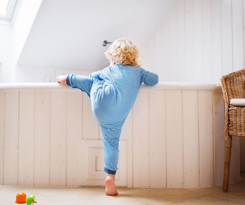 A toddler in blue striped pajamas climbs into a white bathtub.