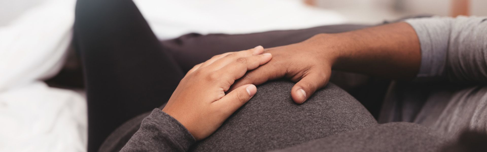 A close-up of two hands resting on a pregnant belly during the second trimester.