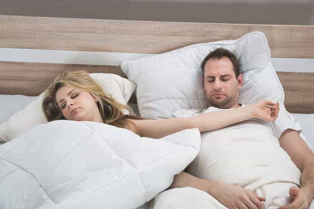 A man and a pregnant woman sleeping in bed. The woman’s arm is draped across the man’s chest.