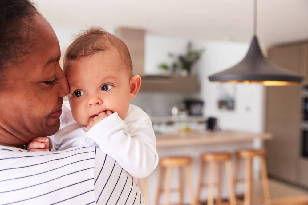 Close-up of a smiling mother holding her infant in a kitchen.