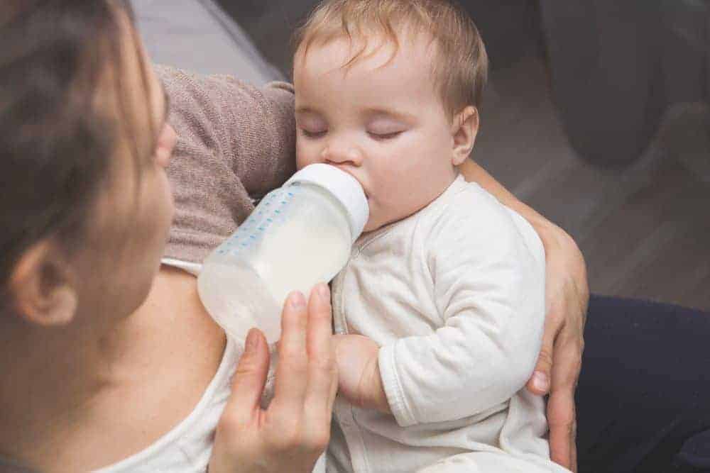 A person cradling a baby while bottle-feeding them with breastmilk.