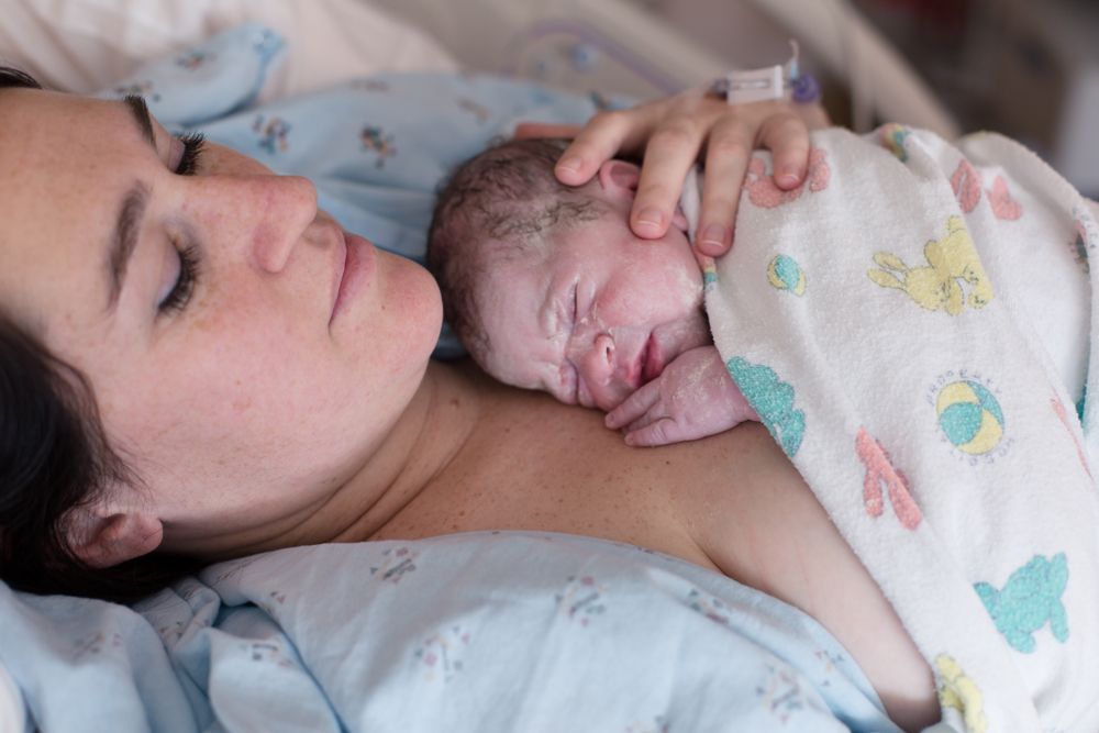 A woman newborn skin-to-skin in a hospital bed after birth.
