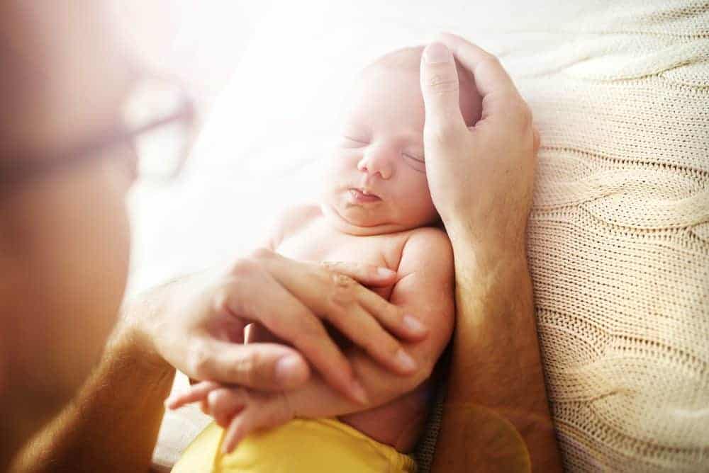 Close-up of a sleeping newborn baby being cradled in an adult's hands against a soft knit blanket.