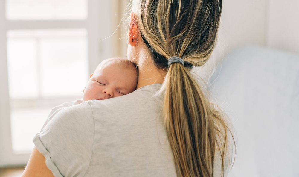 A sleeping infant rests its head on a woman's shoulder.