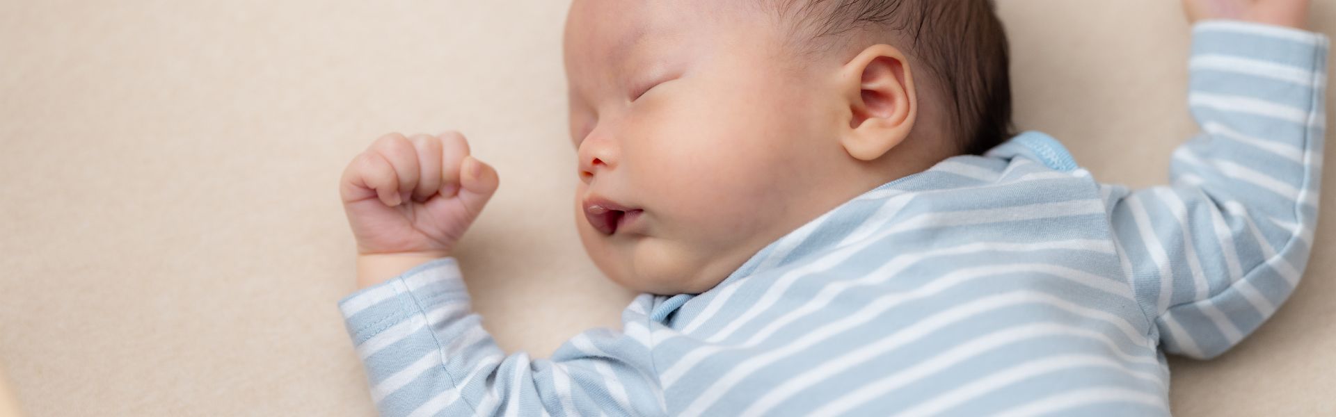 Close-up of a sleeping newborn baby in a blue and white striped onesie.