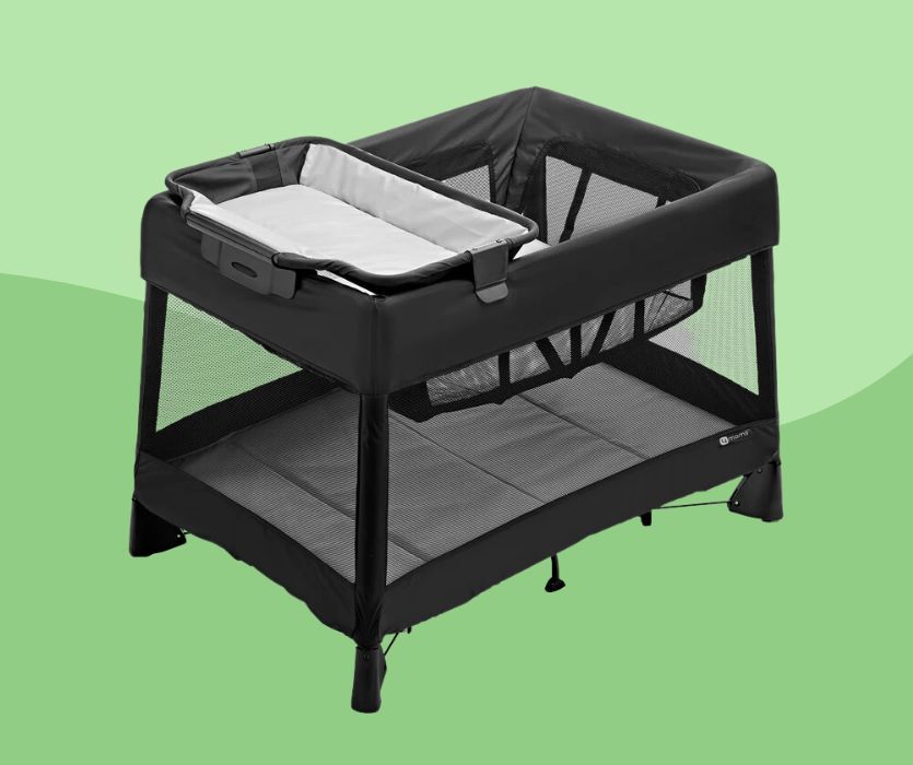 Black portable playard with mesh sides, an elevated bassinet, and a removable changing station on a green background.