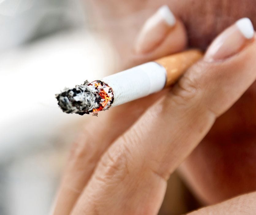 Extreme close-up of a person holding a lit cigarette with burning ash to their mouth.
