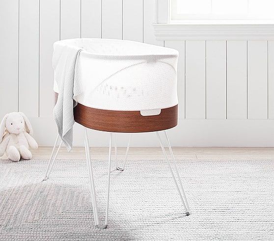 SNOO Smart Sleeper Bassinet with white mesh, wood base, and hairpin legs next to a plush bunny in a nursery.
