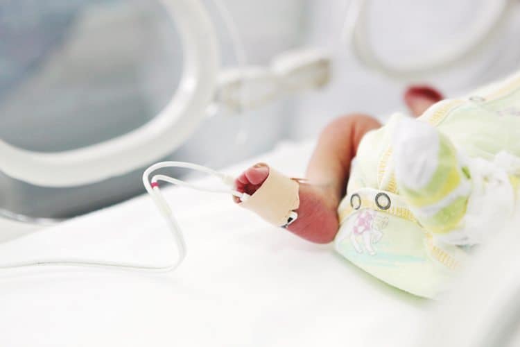 A newborn baby's foot with a monitoring sensor attached, resting inside a hospital incubator.