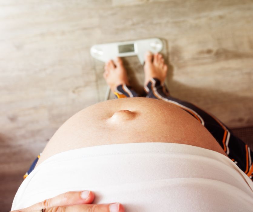 Top-down view of a pregnant person's belly as they stand on a bathroom scale.