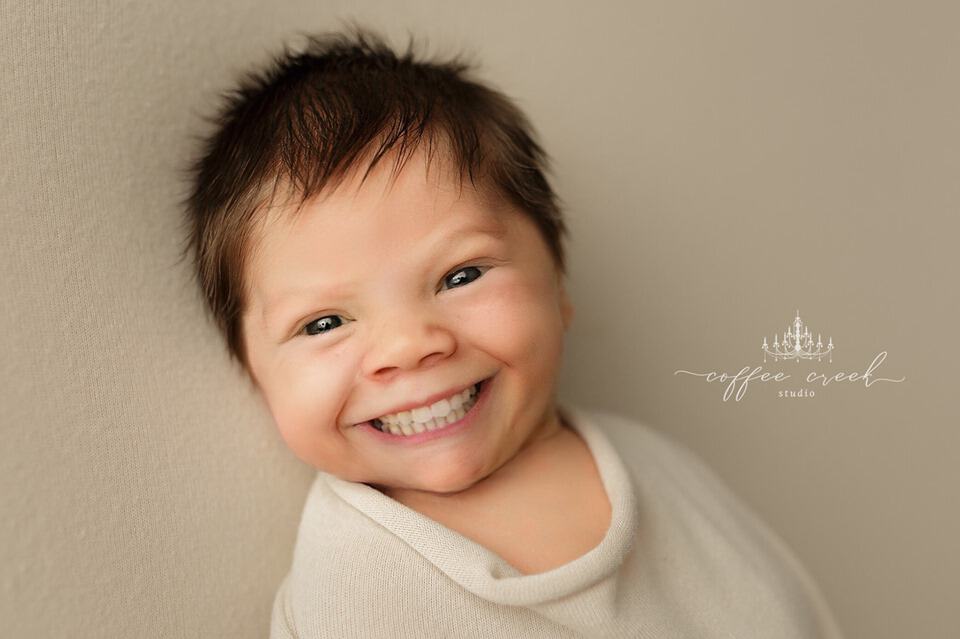 An edited portrait of a newborn baby with a full set of adult-like white teeth smiling at the camera.