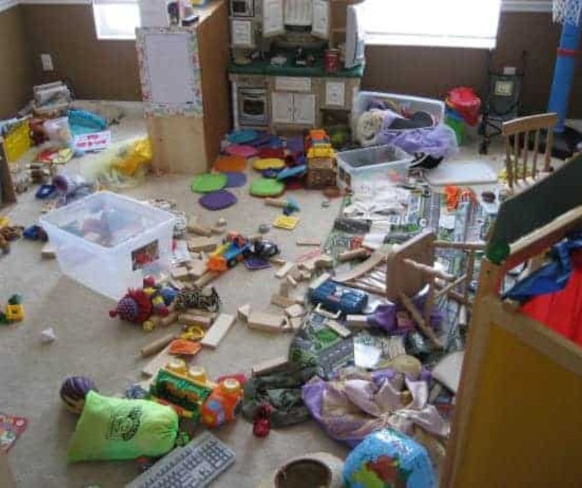 A cluttered playroom floor covered in toys, blocks, and storage bins next to a toy kitchen and play area.