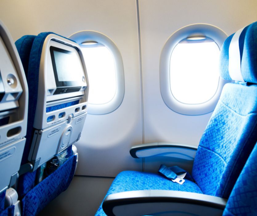 Blue patterned airplane economy class seat next to two bright cabin windows.