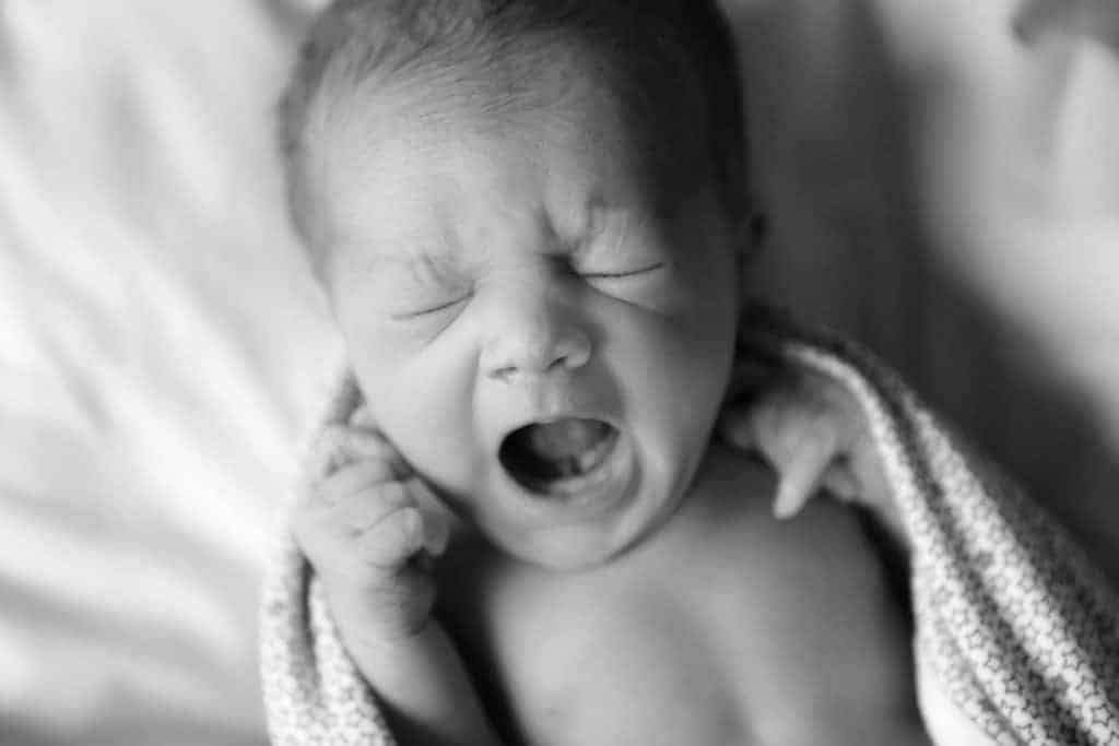 Close-up of a crying newborn baby with an open mouth, showing a heart-shaped tongue tip indicative of tongue-tie.