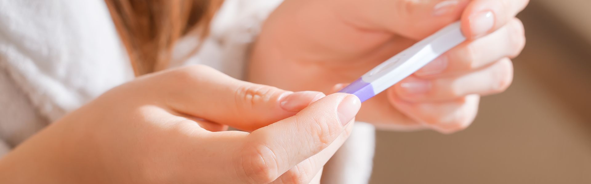 Close-up of a person's hands holding a white and purple home pregnancy test stick.