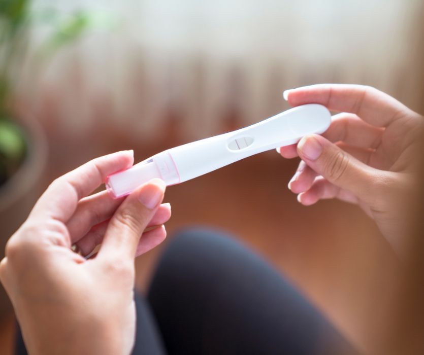 Hands holding a white and pink plastic pregnancy test showing two pink vertical lines.